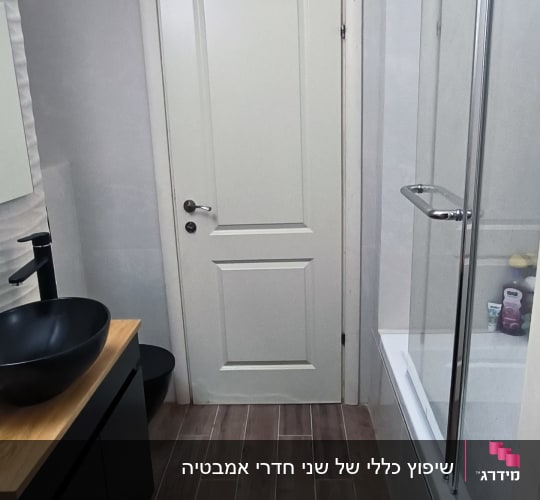 חדר אמבטיה משופץ עם כיור שחור ודלת לבנה